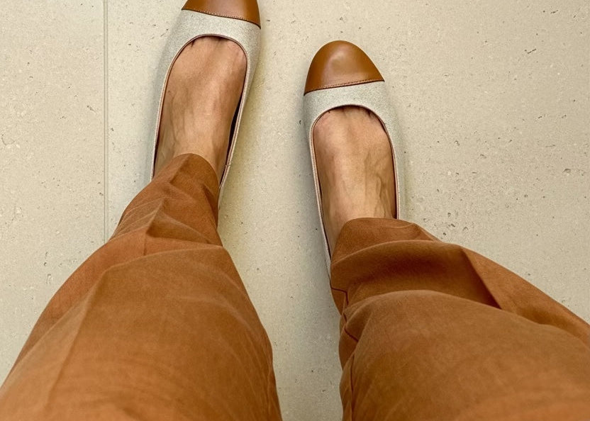 Frau trägt braune Cap-Toe-Ballerinas, eine passende braune Hose und ein weißes Hemd.