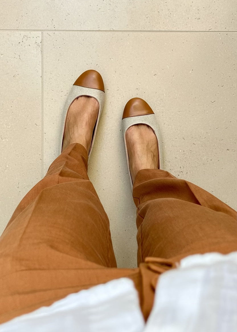 Frau trägt braune Cap-Toe-Ballerinas, eine passende braune Hose und ein weißes Hemd.