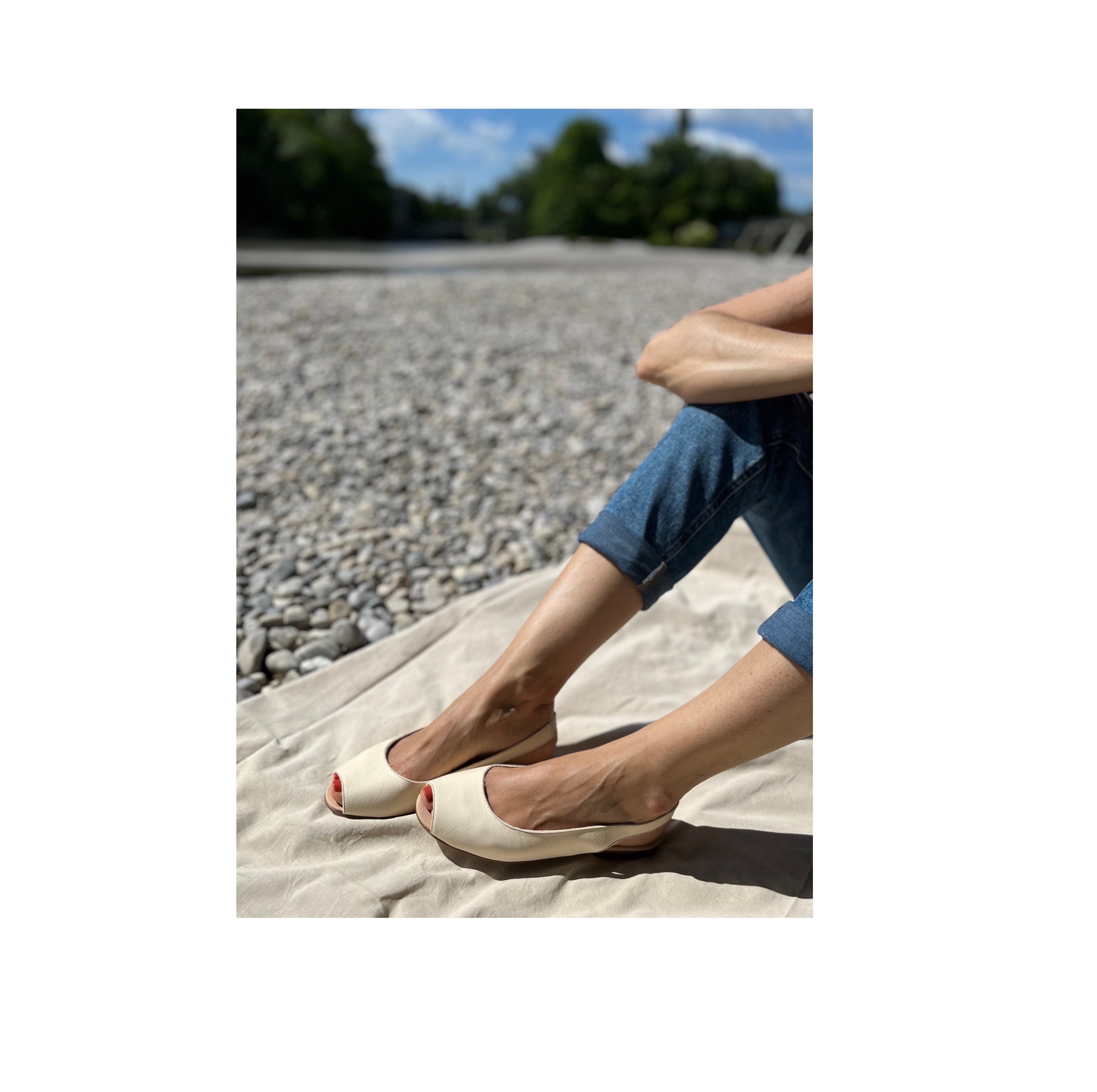 Eine Frau an der Isar trägt cremeweiße Peep-Toe-Ballerinas aus Leder