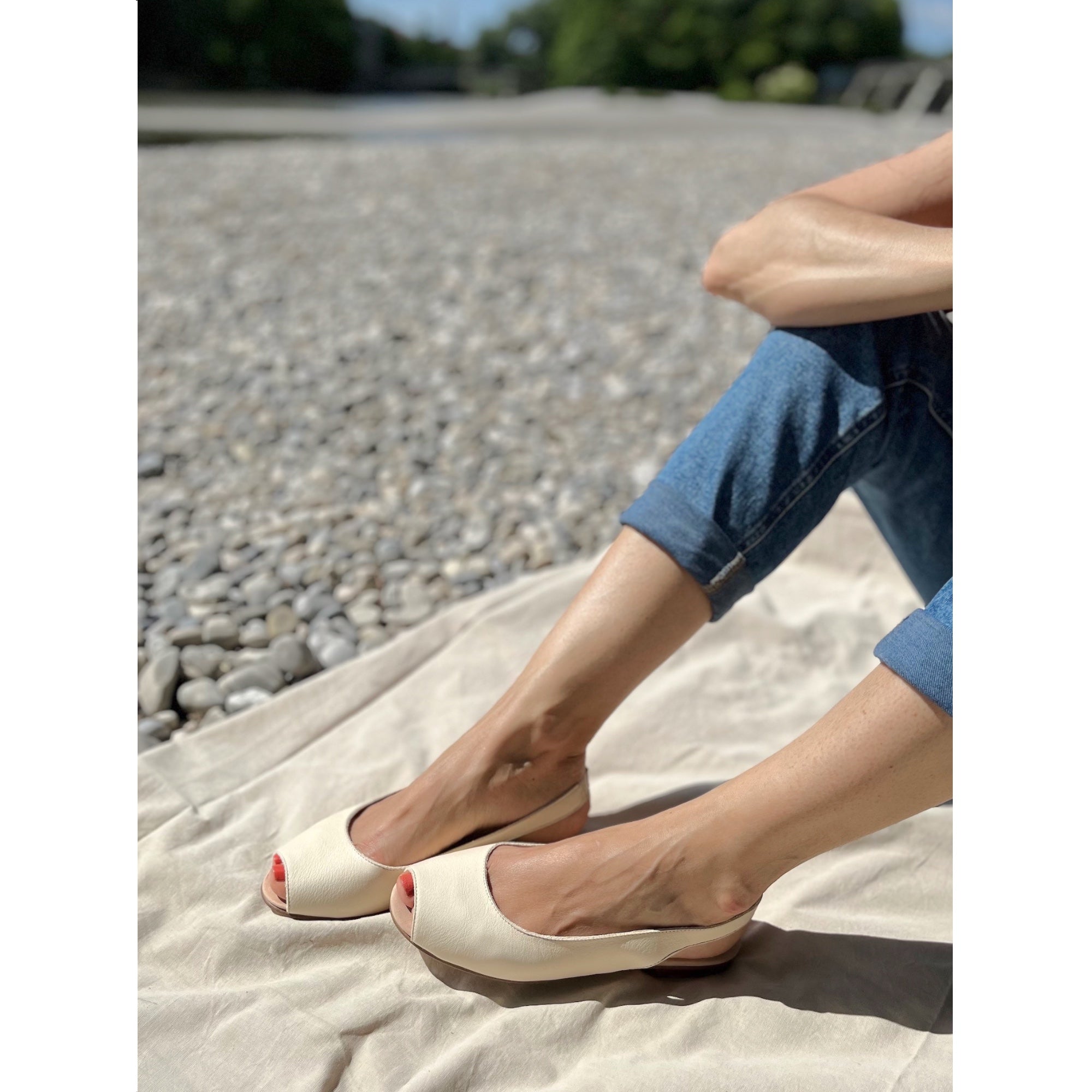 Eine Frau an der Isar trägt cremeweiße Peep-Toe-Ballerinas aus Leder