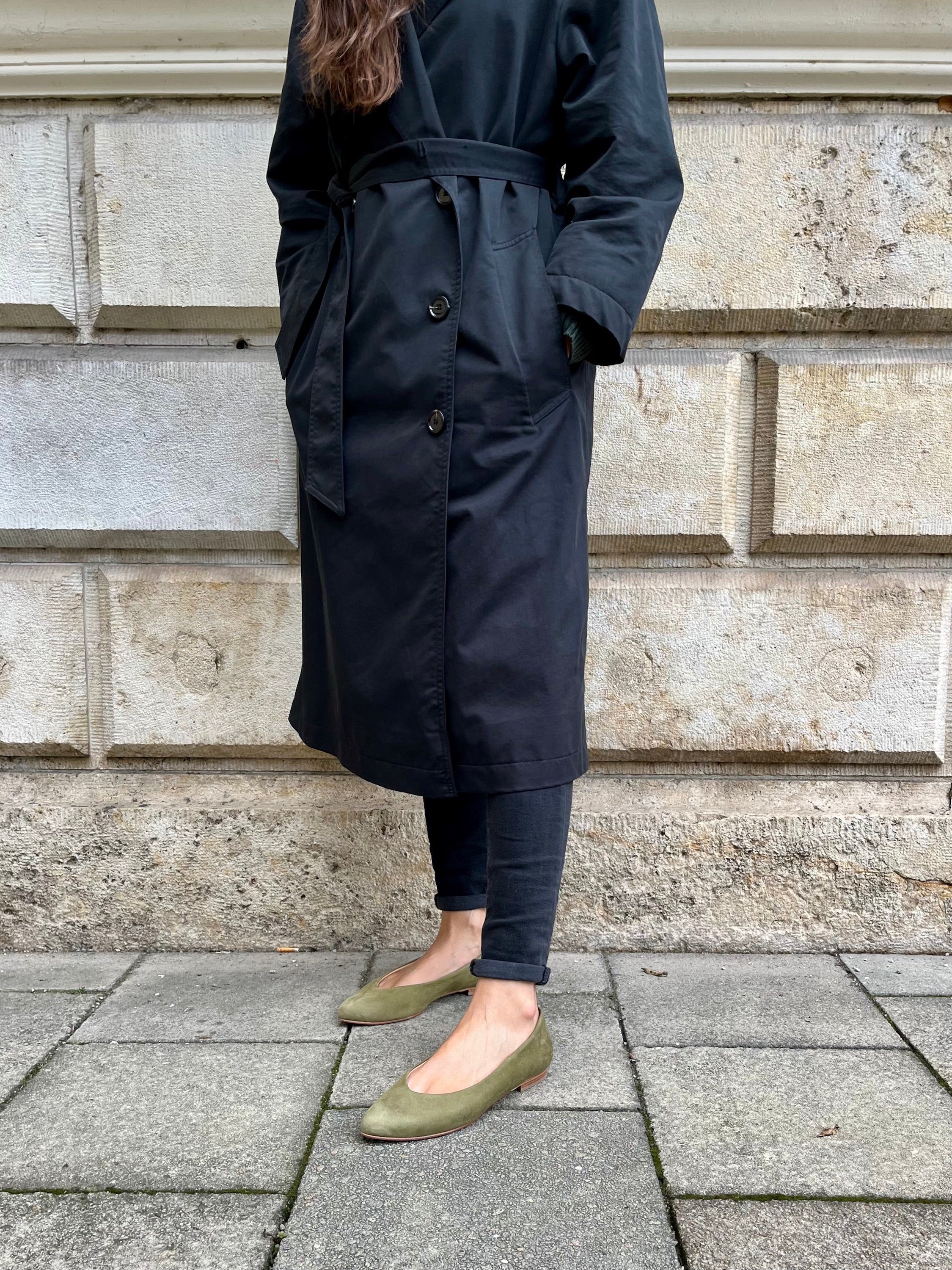 Frau trägt einen schwarzen Trenchcoat und olivgrüne Lederballerinas